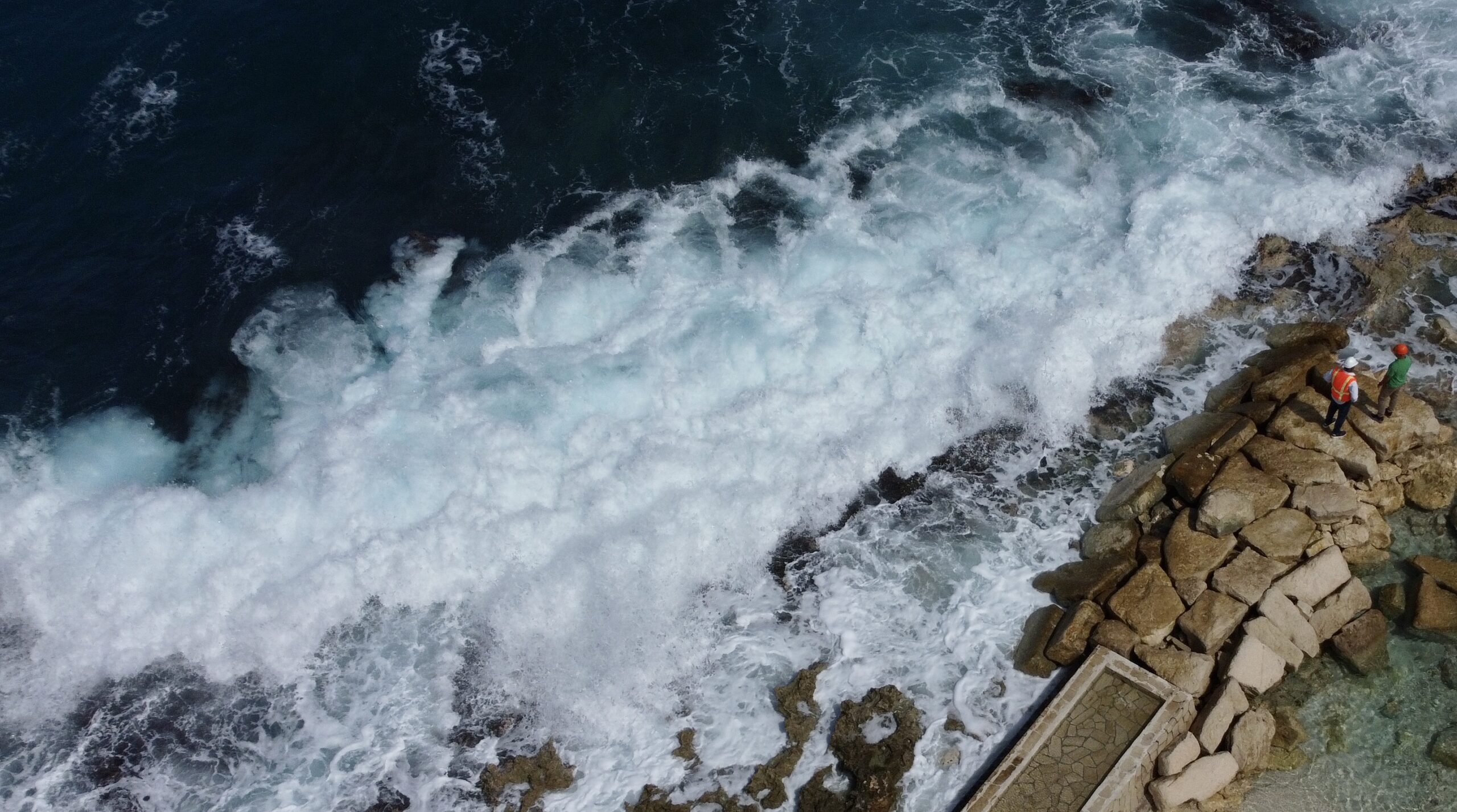 Large waves from a north swell pound the outer side of a protective groyne Feb 2024